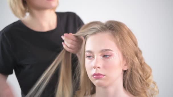 Δημιουργία χτενίσματα σε ένα νεαρό κορίτσι με ξανθά μαλλιά. — Αρχείο Βίντεο