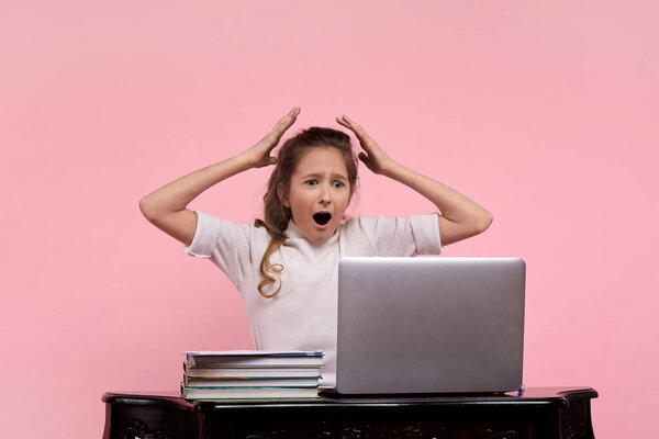 A young girl in a white shirt and blue jeans sits at a computer cursing,