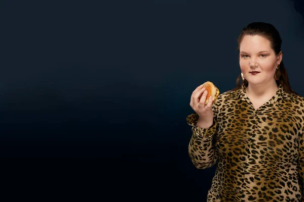 Mädchen in Leopardenbluse mit einem Hamburger in der Hand. Leerstand auf der linken Seite — Stockfoto