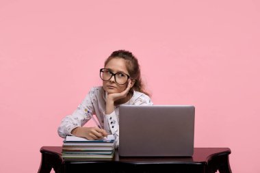 Pembe arka planda genç bir kız öğrenci beyaz bir dizüstü bilgisayarın yanında çalışıyor..