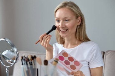 Mutlu esmer, elinde yüzü için bir allık paleti tutuyor..