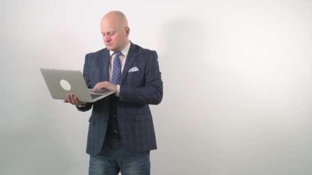 A bald man holds a laptop with a surprised face and asks questions. — Stock Video