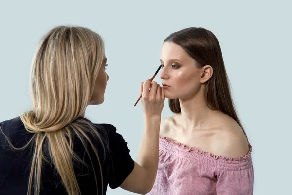 The girl works as a make-up artist and makes a beautiful make-up client. — Stock Photo, Image