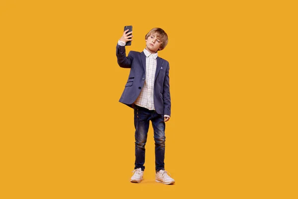 Un chico de cuerpo entero con un traje de negocios se toma una selfie con un teléfono en las manos . —  Fotos de Stock