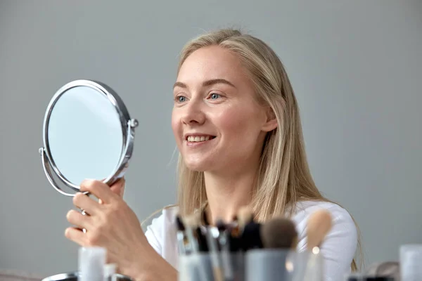 Молодая женщина делает себе макияж дома перед круглым зеркалом . — стоковое фото