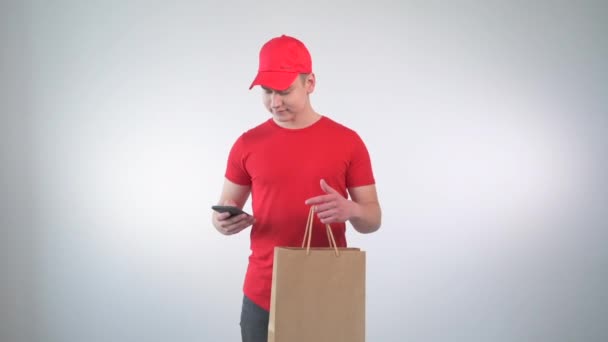 Killen kurir jämför leveransadressen i mobilen och ler mot kameran. — Stockvideo