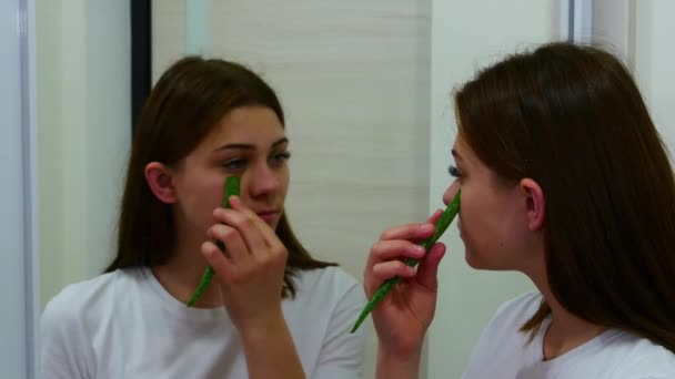 Mujer mirando en el espejo y utilizando hoja de aloe vera — Vídeo de stock