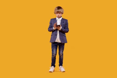 Takım elbiseli, beyaz tişörtlü, elinde telefon olan tatmin olmuş bir çocuk..