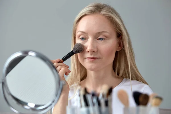 Jovem loira em casa na frente de um espelho faz-se maquiagem — Fotografia de Stock