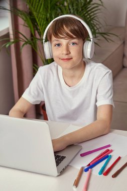 Masada oturmuş ödev yapan gülümseyen çocuk. Kameraya bak..