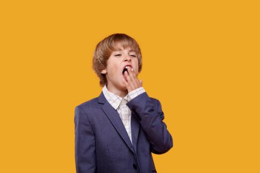 Beyaz gömlekli, gri ceketli sarışın çocuk yorgun ve esniyor..