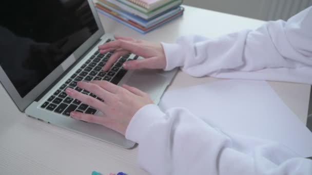 Ένα νεαρό κορίτσι πληκτρολογεί κείμενο σε ένα φορητό υπολογιστή. Χωρίς πρόσωπο. Στο τραπέζι είναι ένας φορητός υπολογιστής — Αρχείο Βίντεο