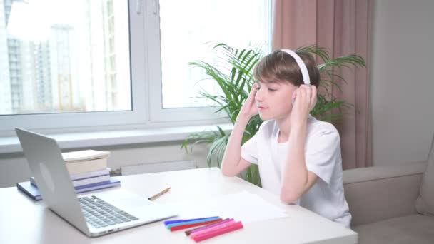 Widok z boku chłopca słuchającego muzyki na słuchawkach i patrzącego na laptopa. — Wideo stockowe