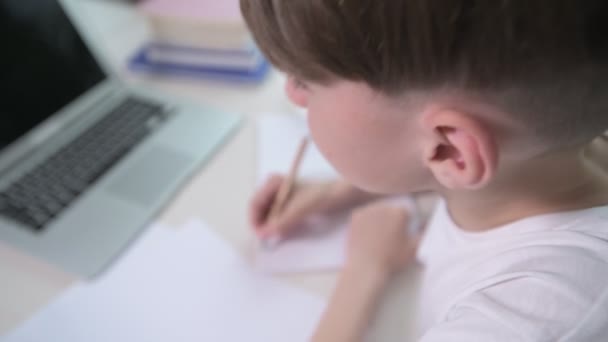 Το αγόρι από κοντά γράφει μια διάλεξη σε ένα άδειο σημειωματάριο. Η θέα από πίσω. — Αρχείο Βίντεο