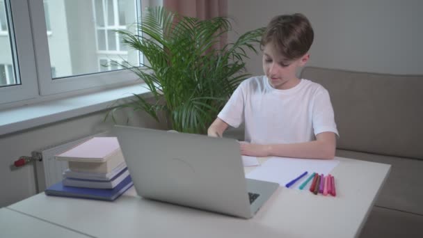 Leuke jongen schrijft een lezing in een leeg notitieboekje. Online slagen voor de cursus. — Stockvideo