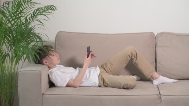 Adam bej bir kanepeye uzanıp telefona bakıyor.. — Stok video