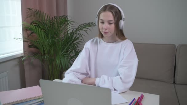 A beautiful girl is trained at home online with headphones on her head. — Stock Video