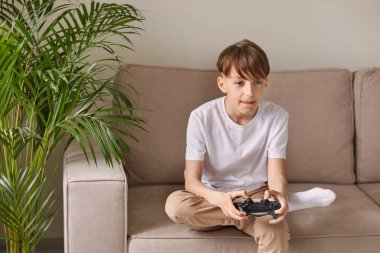 Heyecanlı bir çocuk elinde joystickle video oyunları oynuyor.