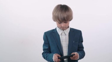 Ciddi bir yüz ifadesi olan beyaz tişörtlü bir çocuk cep telefonunda oynuyor..