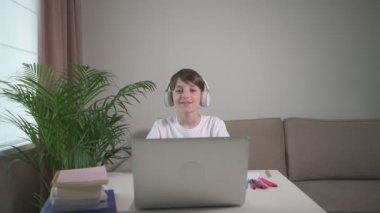 Kablosuz kulaklıklı yakışıklı bir çocuk çerçeveye bakıyor. Çevrim içi eğitim.