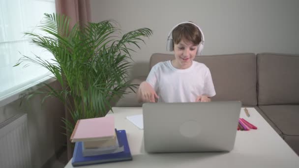 Um garoto sorridente e alegre olha para o laptop e acena com a cabeça. Treinamento online . — Vídeo de Stock