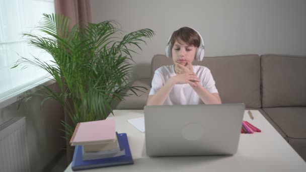 Een jongen kijkt bedachtzaam naar het laptopscherm. Terug naar school. Online opleiding. — Stockvideo