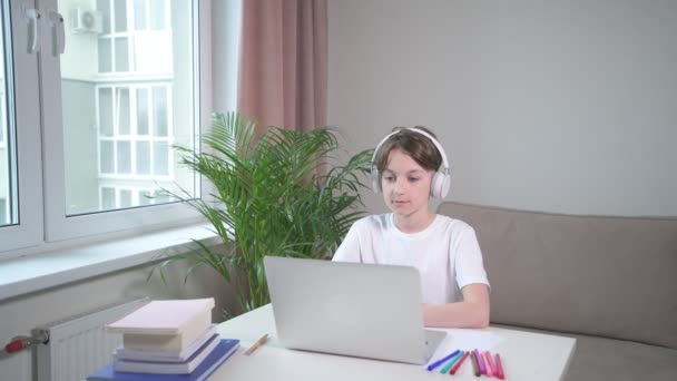 Egy fiú fülhallgatóban otthon tanul egy laptopon.. — Stock videók