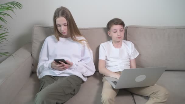 아이들은 집에서 노트북을 들고 손에 전화기를 들고 앉아 있습니다. — 비디오
