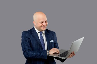 Sağlam, kel bir adam elinde dizüstü bilgisayarla güler..