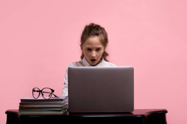 Şaşırmış yüzlü bir kız beyaz bir dizüstü bilgisayara bakıyor..