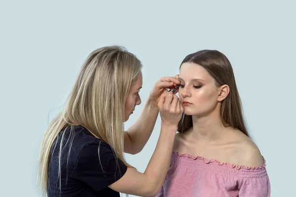 Dziewczyna make-up artysta maluje dziewczynę klient z atramentem do oczu. — Zdjęcie stockowe
