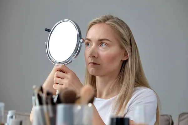 Блондинка делает макияж перед зеркалом, рисует брови карандашом — стоковое фото