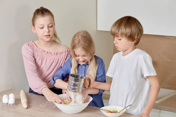 Cute beautiful children with blond hair are preparing pizza dough.