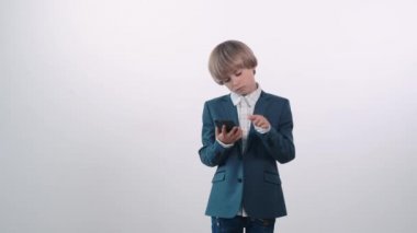 Şaşkın sarışın çocuk elinde bir cep telefonu tutuyor..