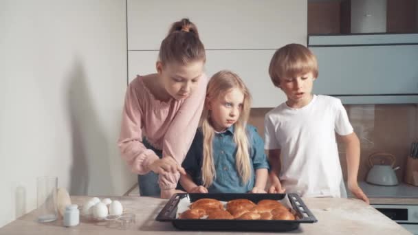 Kis gyönyörű gyerekek állnak a konyhában friss és sült zsemle mellett.. — Stock videók