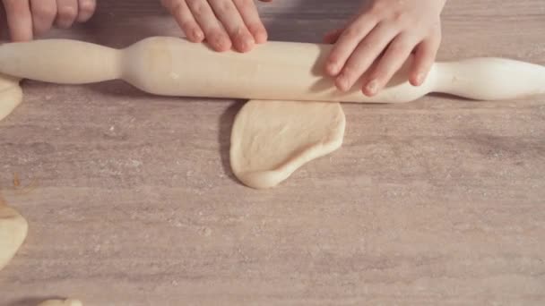 Gros plan des mains des enfants déroulant la pâte pour les biscuits sur une table en bois . — Video