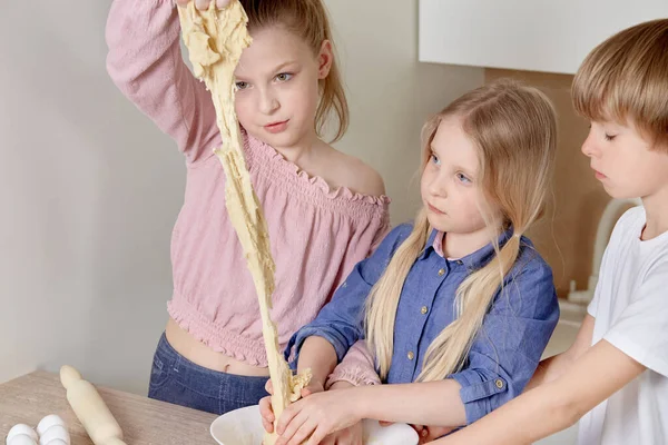 Funny cheerful children cook pizza in the kitchen. Children knead the dough.