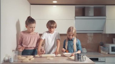 Çocuklar mutfakta sarışın aşçı. Hamuru merdaneyle yuvarla..