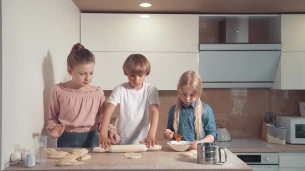 A gyerekek szőkén főznek a konyhában. Gurítsd ki a tésztát egy sodrófával.. — Stock videók