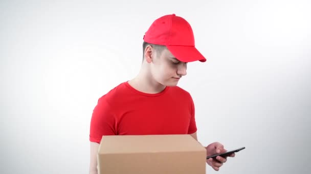 Young guy from a delivery service holds a box in his hands, talks on the phone. — Stock Video