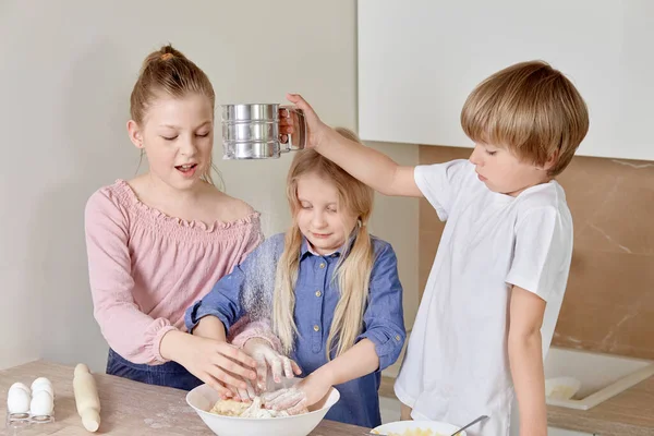 Funny cheerful children cook pizza in the kitchen. Children knead the dough.