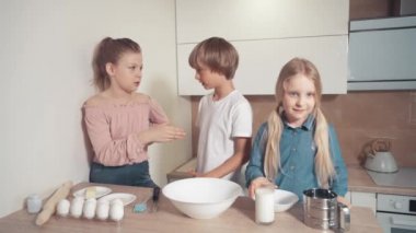 Üç çocuk anneme mutfakta yemek pişirmede yardım ediyor. Bir kız tabağa süt döker.