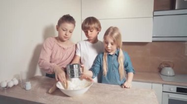 Üç güzel çocuk mutfağa yardım eder ve hamuru beyaz bir tabakta karıştırır..