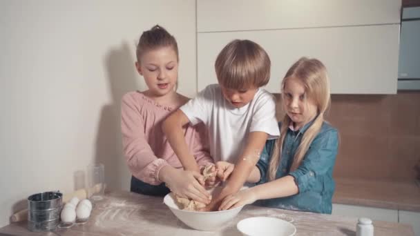 Lindos niños rubios preparan masa de pastel en la cocina. Amasar la masa . — Vídeos de Stock