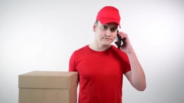Teslimat servisindeki adam elinde bir paket tutuyor ve telefonla konuşuyor..