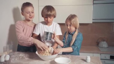 Tatlı çocuklar, bir oğlan ve kızlar, sarışınlar mutfakta turta için hamur hazırlıyorlar..