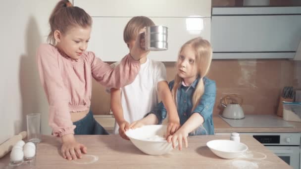 Los niños lindos aprenden a cocinar masa. Añadir harina a la masa. Harina tamizada — Vídeos de Stock