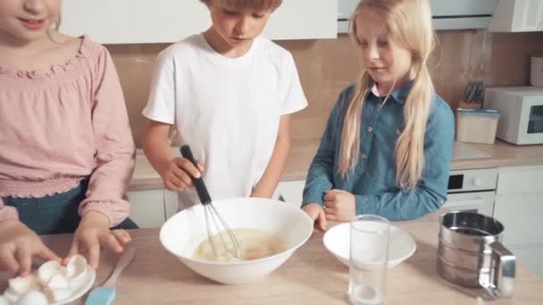 Bonito lindas crianças loiras estão cozinhando massa juntos. Bata ovos em prato . — Vídeo de Stock