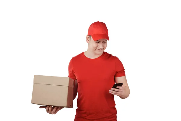 A guy in a red uniform with a parcel in his hand looks at his smartphone. — Stock Photo, Image