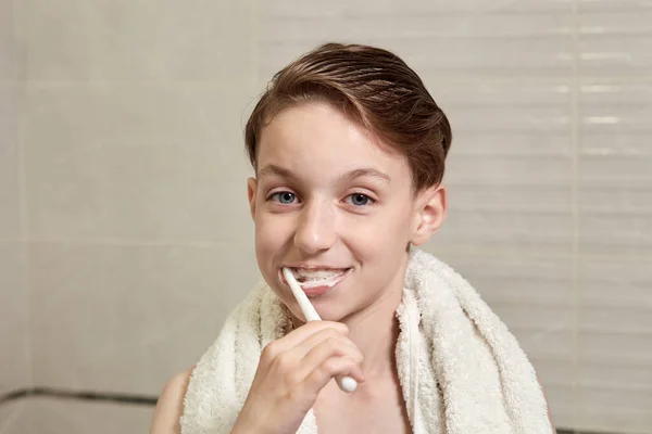 Sonriente chico lindo es cepillarse los dientes en el baño con una pasta . — Foto de Stock